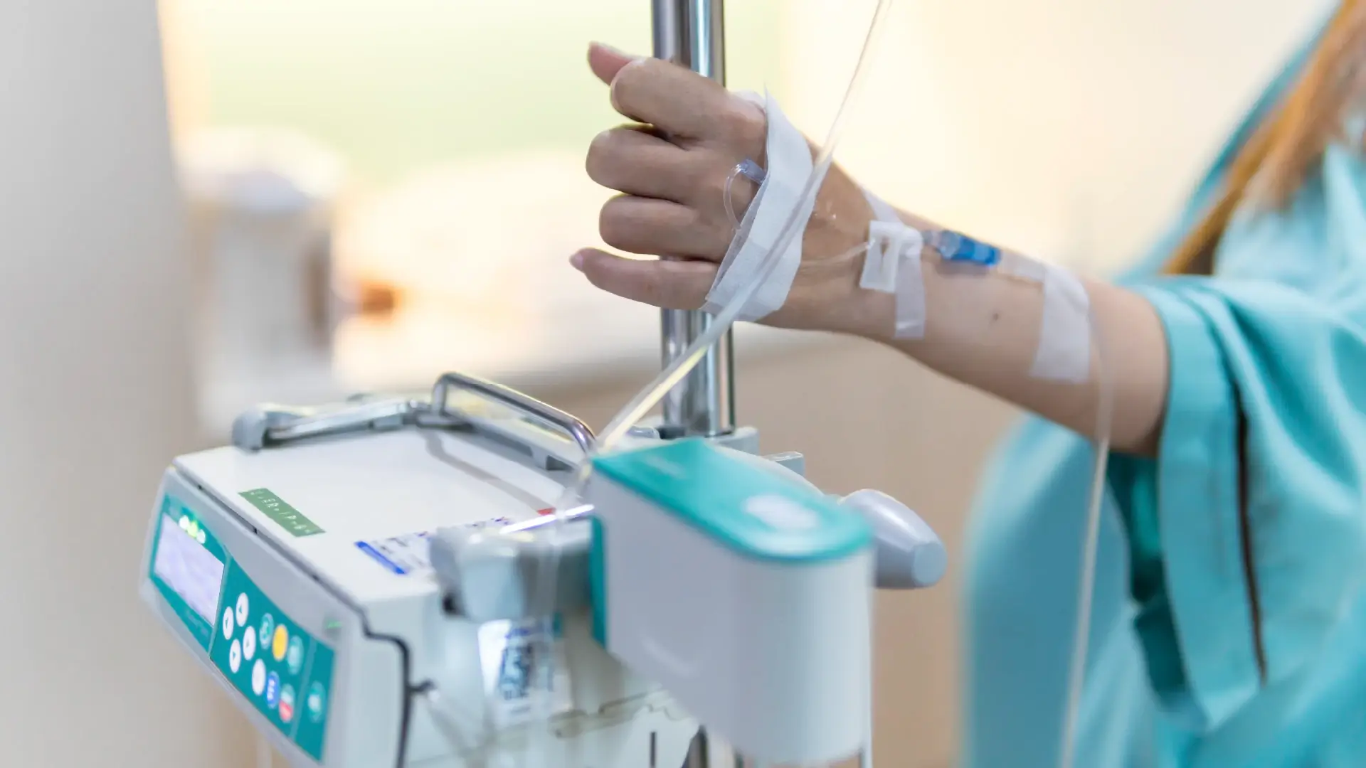 A patient's hand holding IV pole with infusion pump at bottom