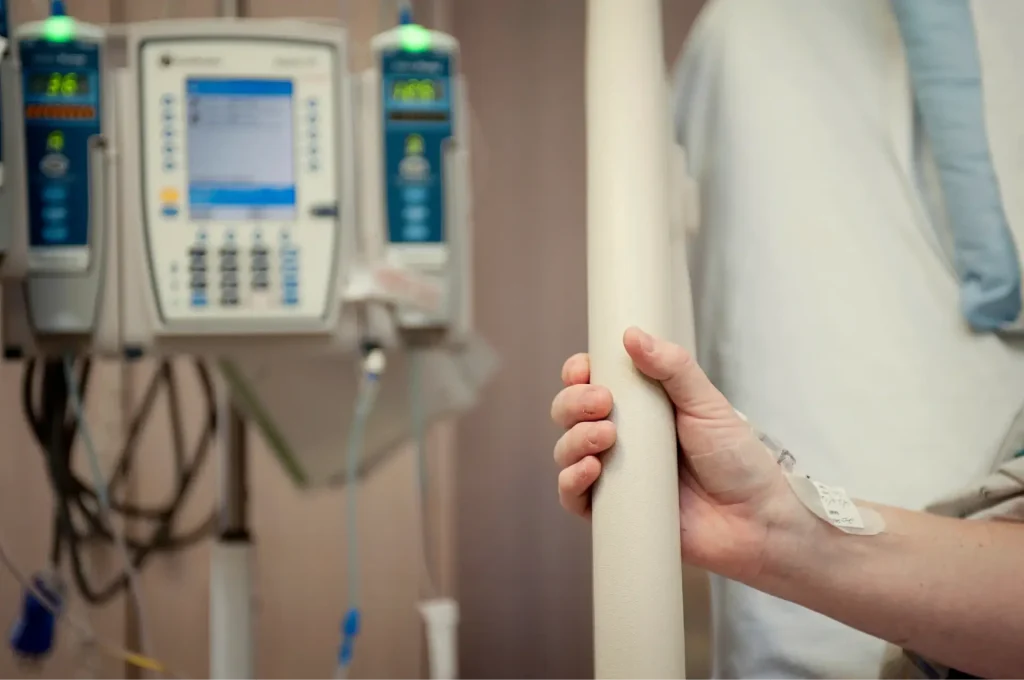 woman gripping hospital bed with hand with infusion pump in background